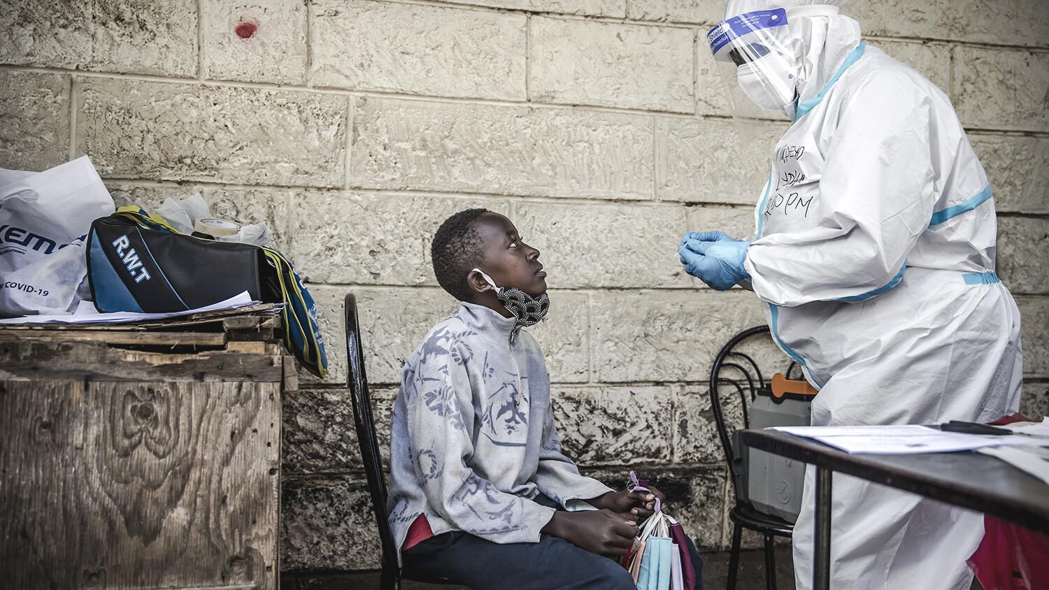 A kid selling face masks in the street and a health worker wearing a hazmat suit.